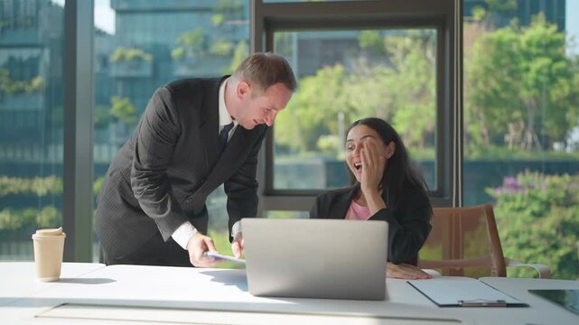 Unexpected Moment in the Office: A man and woman share a candid moment over the office work as sunlight streams through the windows.