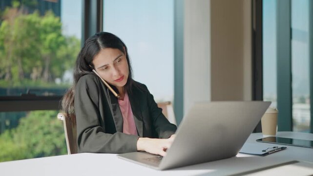 Multitasking Moment: A dedicated professional juggles multiple tasks simultaneously, engrossed in a phone call while focusing on her laptop, a testament to her efficiency and commitment.