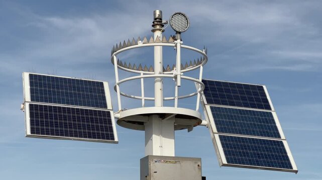 Close-up view of weather station featuring solar panels, anemometer with navigation light, and meteorological sensors against blue sky, technical environmental monitoring equipment.