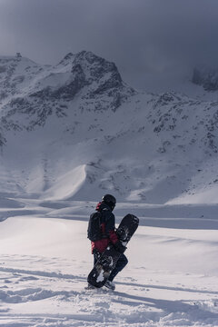 Snowboarded carrying snowbard on a background of dramatic peaks