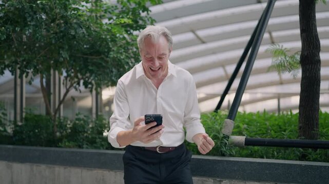 Happy Moments of a Man with Phone: Capturing the elation of an older man engrossed in his mobile phone, his expression radiating joy and excitement. Amidst an urban setting.
