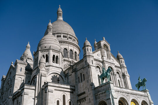 Sacr&eacute;-C&oelig;ur Basilica in Montmartre, Paris, France, showing the white domes and Romano-Byzantine architecture under a clear blue sky with the equestrian statues at the entrance.