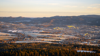 Fototapeta premium A view of Liberec during a winter morning. The landscape shows mountains in the background and fields covered in snow. The town is partly visible with buildings and trees in the foreground.
