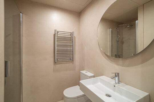 Modern bathroom with a round mirror, white sink, and shower. Neutral tones create a clean and minimalist atmosphere.