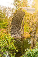 Fototapeta premium Rakotz Bridge gracefully arches over calm waters, mirrored perfectly against a backdrop of fall foliage. Germany