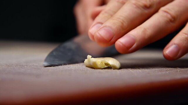 Garlic clove being crushed on wooden cutting board with kitchen tools nearby