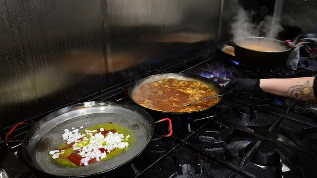 Chef cooking multiple paellas on a professional gas stove