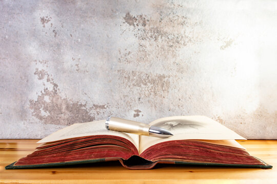 Bullet on a opened vintage book with red pages ona wooden desk, religious killings concept