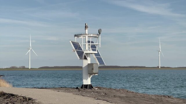 Zierikzee, Zeeland, Netherlands - March 17, 2026: Weather station with solar panels and anemometer at Zeelandbrug area, De Val sublocation, multiple wind turbines visible in background across water.