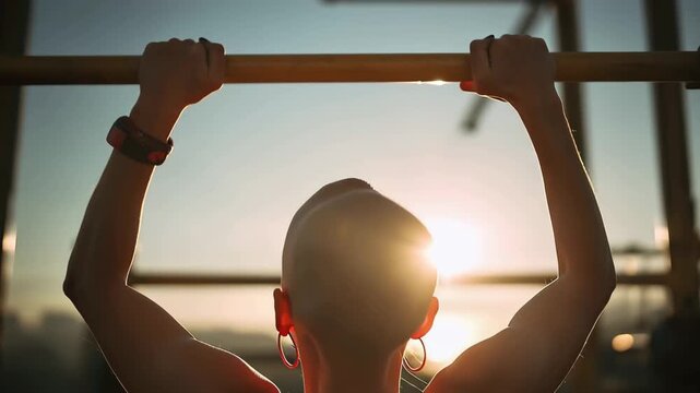 Strong person does pull-ups at sunset in a gym, showing determination and focus in their workout routine, with sun shining in the background