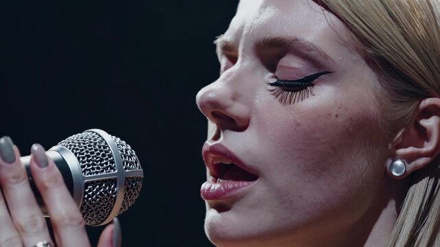Female singer performs with passion in studio. Close-up of vocalist expressing emotions through music. Intimate atmosphere elevates live performance experience.