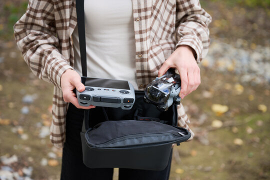 Woman holds drone and controller taken from bag. Close up of hands preparing quadcopter outdoors, organizing gear before flight, concept of hobby, readiness and technology
