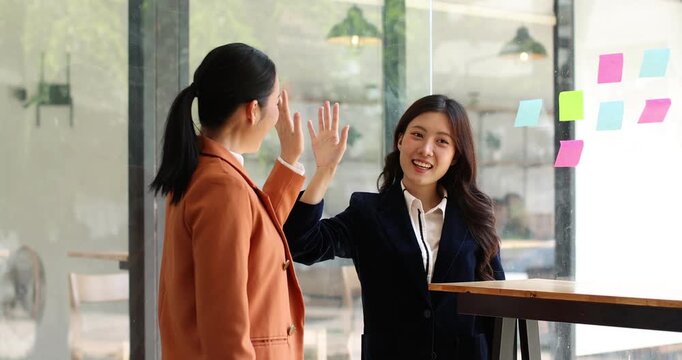 The image captures two women in blazers sharing a high five, showcasing excitement and camaraderie while interacting and engaging in a motivational conversation.
