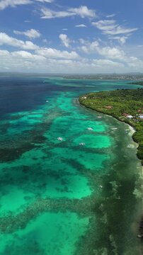 Vertical drone ascends left over reef shallows and coast in Panglao, Bohol