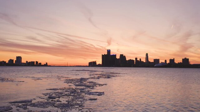 A peaceful winter sunset from Sunset Point in Belle Isle Park as the sun sets behind the Detroit skyline. Golden light reflects across the icy waters of the Detroit River while chunks of ice drift.