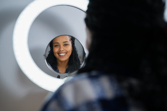Smiling person looking at reflection in mirror with ring light indoors