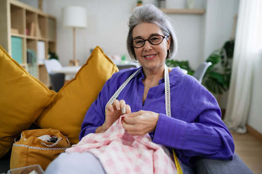 Smiling woman sewing fabric with measuring tape at home