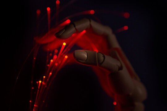 Robotic hand reaching for optic fiber with red neon light in darkness