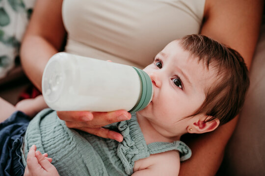 Mother bottle feeding baby on sofa at home enjoying quality time