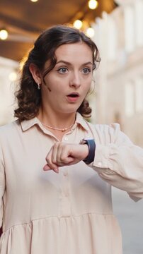 Scared woman worrying to be punctual, with anxiety checking time on watch, running late to work or transport, being in delay, deadline outdoors. Lady tourist walking in city street. Town lifestyles
