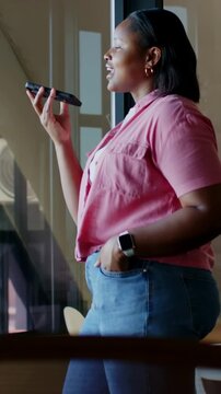 Vertical video: Sliding mullion revealing woman taking call on phone by windows, wearing pink shirt