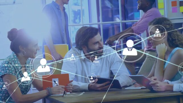 Seated business team using tablets in office, digital user icons expanding over group to show links