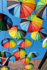 Obraz premium Vibrant rainbow umbrellas suspended under a clear blue sky. A joyful, colorful display perfect for summer, travel, celebration