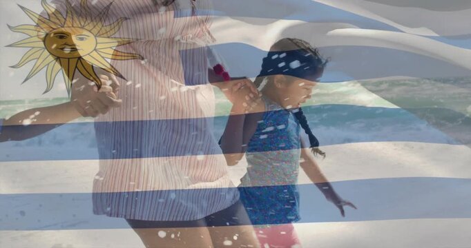 Woman guiding girl on sand, stepping causing surf splashes under Uruguay flag overlay for travel