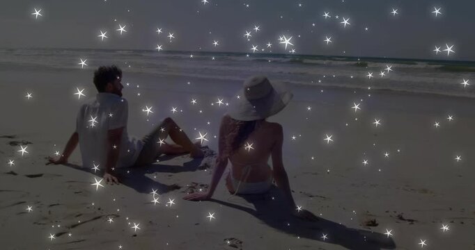 Sparkle overlay appearing, couple on beach, woman in swimsuit adjusting sunhat and watching sea