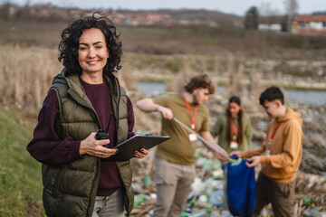 Obraz premium Female volunteer organizer supervising river cleanup with young people