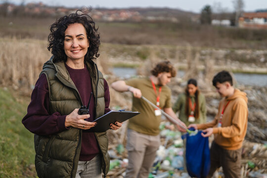 Female volunteer organizer supervising river cleanup with young people