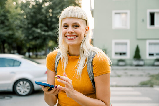 Smiling woman with backpack using mobile phone outdoors at sunset