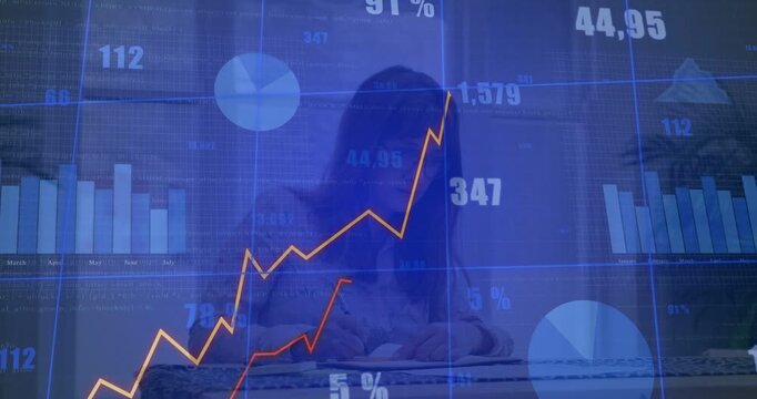 Woman writing at home desk, live finance charts updating over notebook, enabling analytics tracking