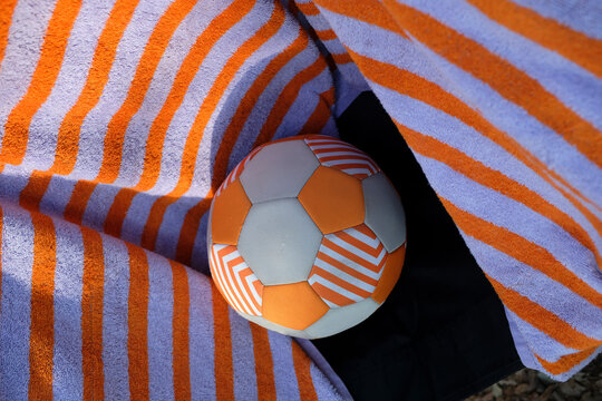 Orange and purple striped towel with football on beach in Corsica