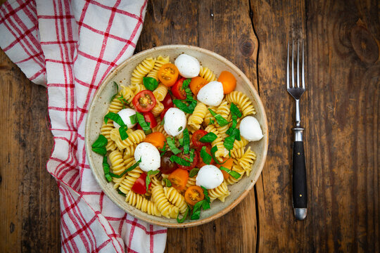 Pasta bowl with mozzarella tomato and basil on rustic wooden table