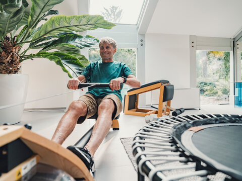 Man exercising on rowing machine at home in modern living room