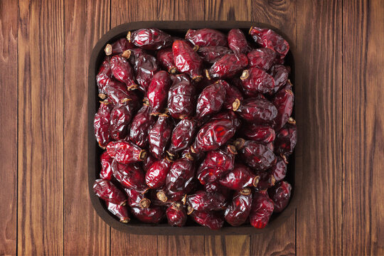 dried rose hips or dogrose berries in square plate on wooden table background. vegetarian organic food for healthy diet.