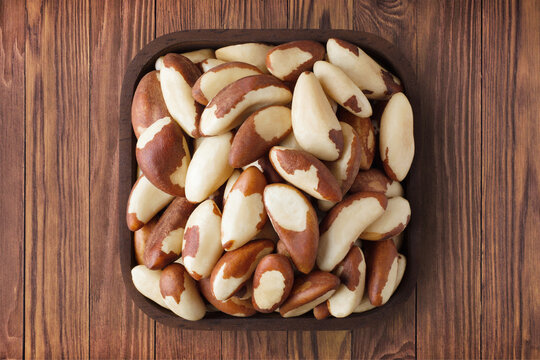 brazilian nuts peeled in square plate on wooden table background. vegetarian organic food for healthy diet.