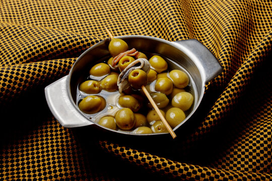 Spanish tapas with olives and anchovy skewers on patterned fabric