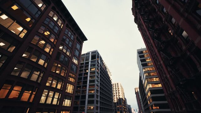 towering glass buildings at twilight, reflections on mirrored facades, bold lowangle composition with grid windows glowing with office light, sharp angular