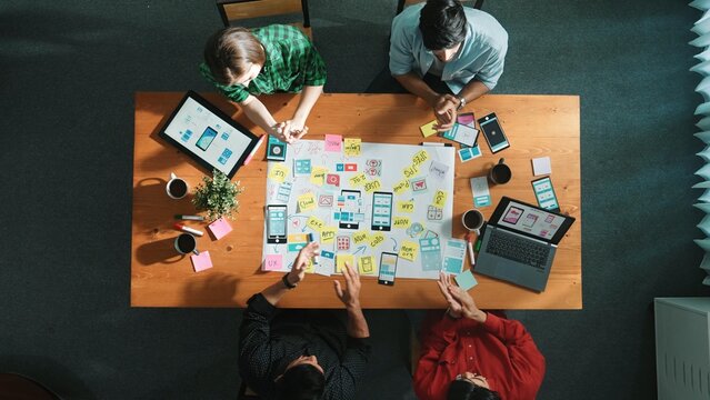 Top view of skilled team putting hand together to celebrate at meeting table while brainstorm idea about Ux, Ui design for mobile phone interface or designing application at meeting room. Convocation.