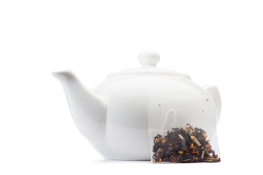 Filter tea bag next to ceramic teapot, isolated on white background.