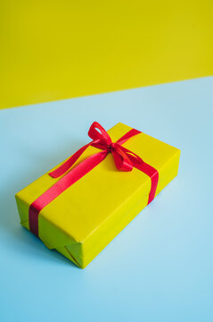Yellow gift box with red ribbon on blue table against yellow background