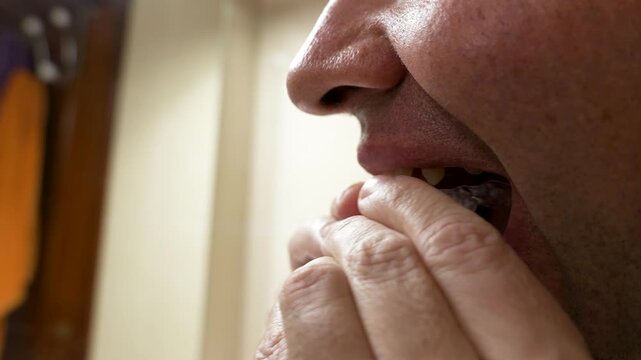 Close-up side view of an adult man placing a clear orthodontic aligner inside his mouth. Concept of modern teeth straightening treatment and personal oral care.