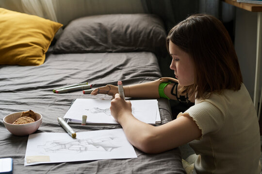 Creative child with prosthesis drawing sketches in bedroom at home
