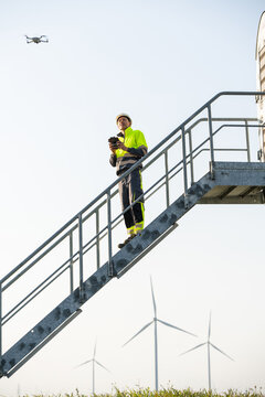 Engineer with drone inspecting wind turbines at wind farm outdoors