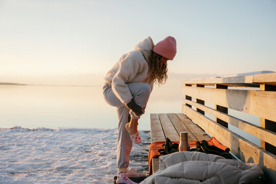 Woman changing clothes by a snowy lake before a winter swim at sunset