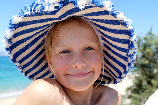 Happy child in striped sun hat smiling at beach on sunny Mediterranean day