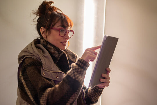 Woman wearing eyeglasses using tablet PC near wall