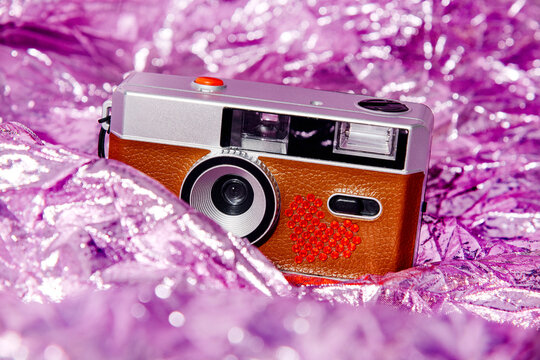 Retro compact camera with glitter heart on metallic magenta background